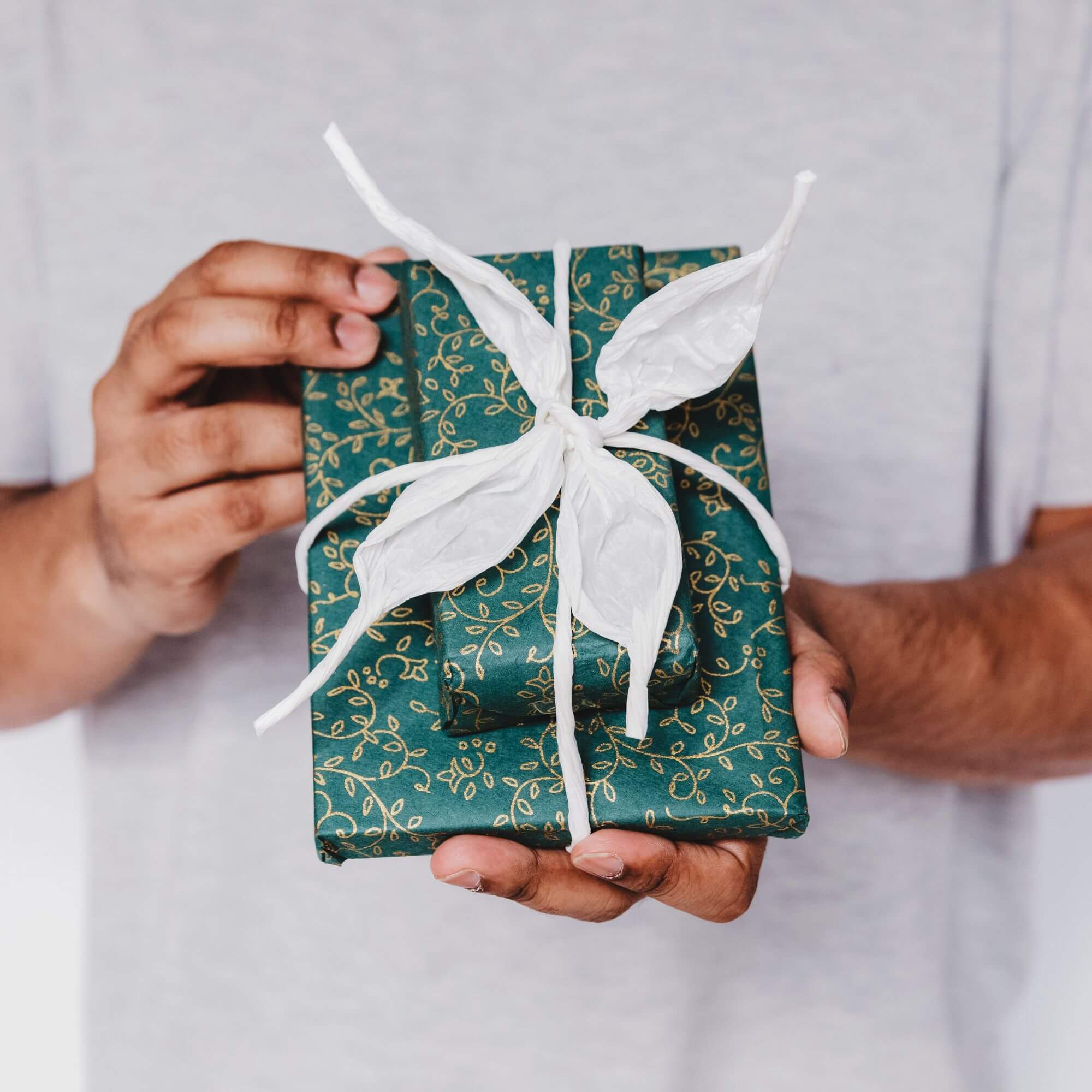 A man holding two gifts wrapped in green wrapping paper and white ribbon.